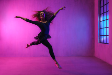 Fototapeta na wymiar Modern dance girl dancer dancing in neon light doing gymnastic exercises in studio, copy space.