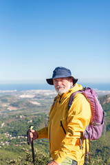Fototapeta na wymiar male elderly hiker with backpack standing on the summit looking at camera