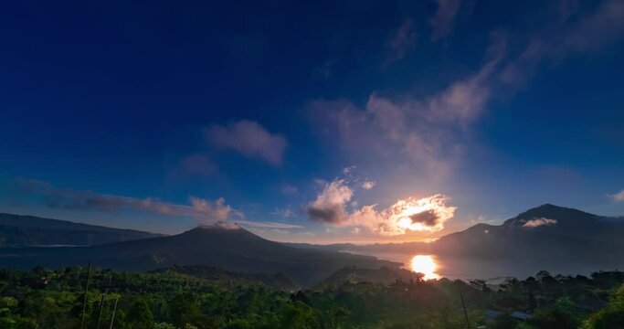 Timelapse of sunrise with view on Batur and Abang volcanoes and lake on Bali. Clouds are moving fast in blue sky, the sun is rising