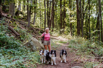 Senior woman walking with her three dogs in forest.