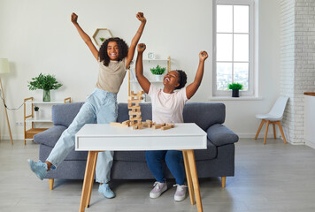 Happy family playing table games at home. Cheerful African American mother and child playing games and having fun together. Joyful, excited little girl celebrating her victory in board game - Powered by Adobe