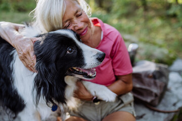 Senior woman resting and stroking her dog during walking in forest.