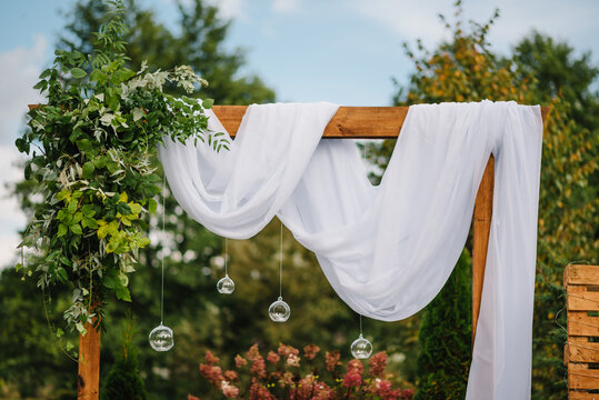 Wooden decor. The wedding arch is decorated with retro garland with bulbs and candles. Outdoor wooden photo zone or wall. Decoration of the ceremony in open air. Sweet and sour rustic style.