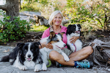 Senior woman having break during walking her three dogs in forest.