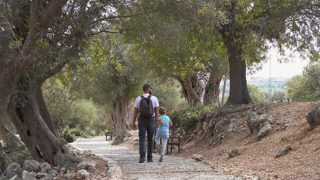 Travel with people. Caucasian father and his child boy or girl walking together path in ancient forest public park summer. Kid happily jumping. Family together leisure time activities.