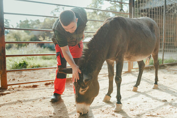 Caretaker with down syndrome taking care of animals in zoo, stroking donkey. Concept of integration...