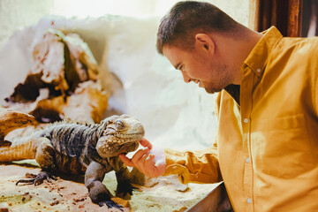 Caretaker with down syndrome taking care of animals in zoo, stroking iguana. Concept of integration...