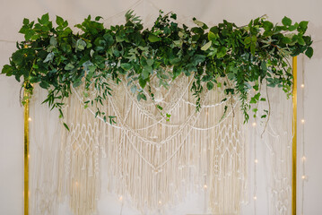 Setup for ceremony. Wedding arch is decorated leaves eucalyptus greenery and garland with lights in tent. Banquet hall with decor herbs. Luxury elegant wall and decoration space, or place for photos.