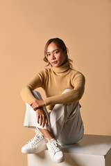 Elegant woman in stylish warm clothes sitting over beige background . Fashion studio photo, Autumn and Winter concept