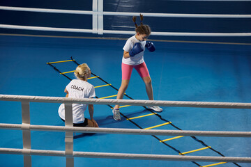 Speed, reaction, pace. Two athletes, little girl, beginner kickboxer training with female coach at...