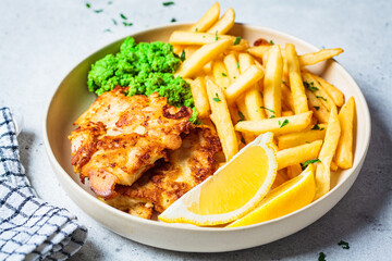 Fish and chips. Cod fish in batter with french fries and mashed peas on a white plate, gray background. English food concept.