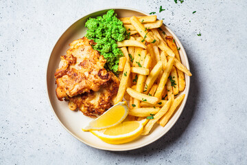 Fish and chips. Cod fish in batter with french fries and mashed peas on a white plate, gray...