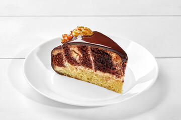 Slice of vanilla and cocoa biscuit cake with sour cream, walnuts, dried apricots and chocolate ganache