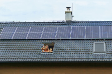 Happy mother and her son waving from skylight window in their new house with solar panels on the...