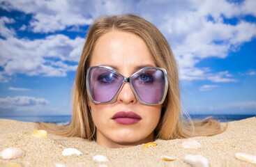 Woman buried in sand on beach with sunglasses