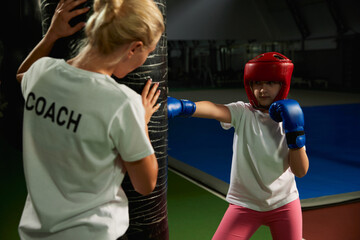 Two athletes, little girl, beginner kickboxer training with female coach at sports gym, indoors. Concept of studying, challenges, sport, hobbies, competition