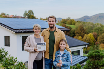 Happy family holding paper model of house with solar panels.Alternative energy, saving resources...