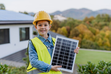 Little girl with protective helmet and reflective vest holding photovoltaics solar panel. Alternative energy, saving resources and sustainable lifestyle concept.