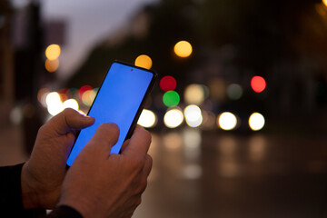 man's hands using cell phone screen outdoors with car lights