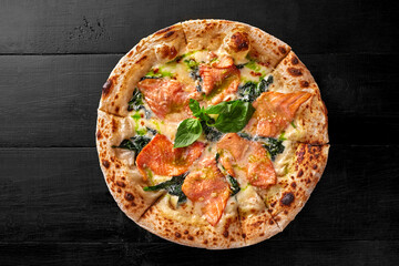 Pizza with cream cheese sauce, salmon, spinach, pesto and fresh basil on black wooden surface