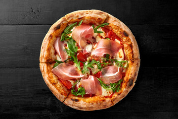 Pizza with pelati sauce, mozzarella, cabanossi, chicken fillet, bacon, prosciutto, arugula on black wooden background