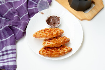 Waffle croissants (also called croffles) coated in melted sugar on a white plate on a white background. with chocolate jam as a complement