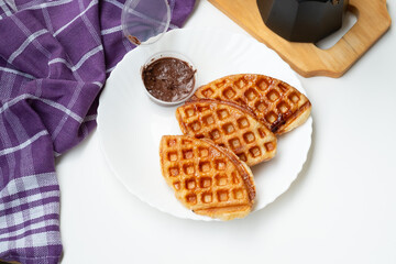 Waffle croissants (also called croffles) coated in melted sugar on a white plate on a white background. with chocolate jam as a complement