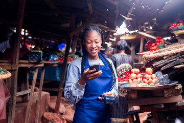 A Young Girl Using her mobile phone in African market holding Pos machine paying bills online smiling