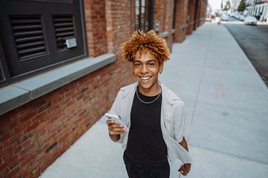 Young positive multiracial man in stylish clothes holding smart mobile phone. Looking at camera