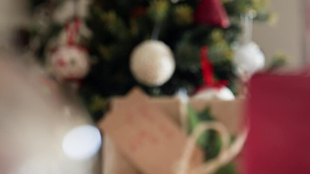 Rack focus from Christmas tree to wrapped gift box with tag FROM ME TO YOU.