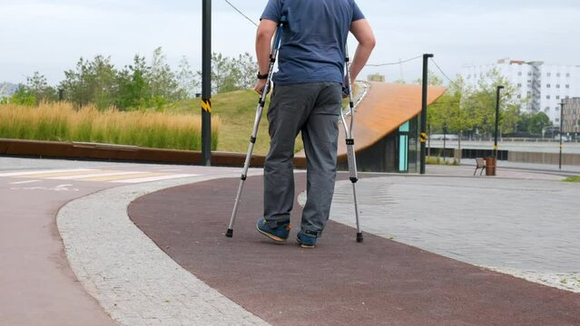 Plus size mature man walks on crutches along a track allocated for running in a city park