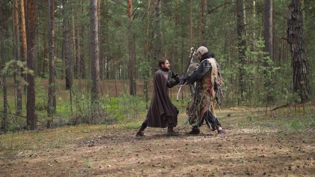 Young knight and angry ogre fight on fir forest glade slow motion. Man in middle aged armour protects land from monster. Fairy tail scene reconstruction