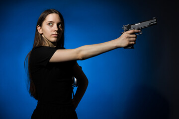 young beautiful woman with long hair in a black t-shirt aims a gun on a blue background