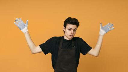 a young man in a black T-shirt and apron in work gloves shyly spreads his arms to the sides