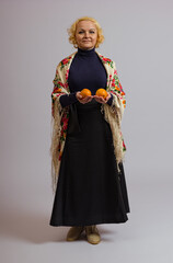 a woman in a traditional colored Russian headscarf holds tangerines in her hands on a white background