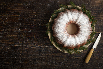 Homemade sponge cake with icing sugar on a background with fir branches. Rustic style. Christmas.