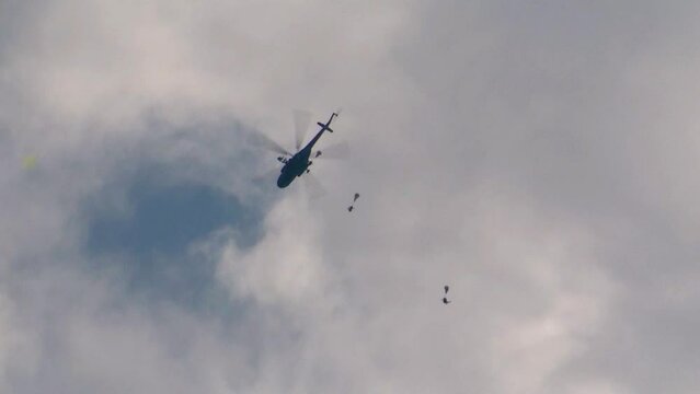 A group of military parachutists jumps out of a helicopter, the canopy of the parachute opens in the air. Concept: airborne assault, military operations, seizure of territory.