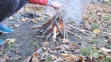 A young man kindles a fire in the woods on the banks of the river