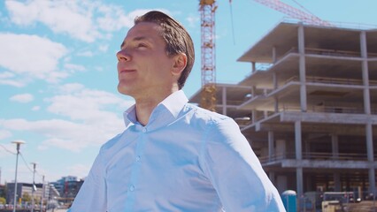 Business person standing in front of construction site. Office building and crane background. Development, real estate and investment.