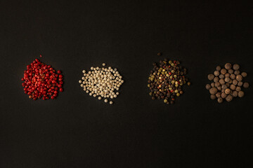 Peppercorns of different varieties on a dark background.