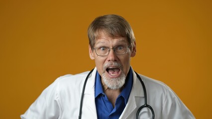 Yes winner gesture. Happy amazed doctor man shocked. Handsome doc in white medical coat surprised looking into camera isolated on yellow background