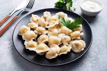 Traditional pelmeni, ravioli, dumplings filled with meat on plate, russian kitchen. Light concrete background, copy space.