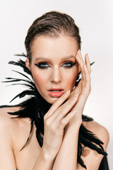 Fototapeta premium Beautiful girl with smoky eyes make-up, plume of black feathers on a white background