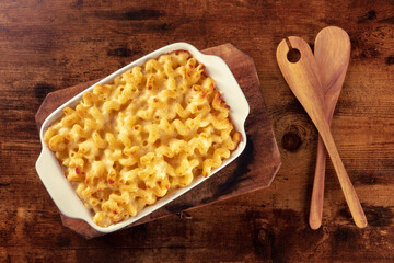 Macaroni and cheese pasta in a casserole, overhead flat lay shot on a rustic background with wooden spoons