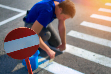 Road service worker paints striped pedestrian crossing on asphalt with paint brush. Markings for...