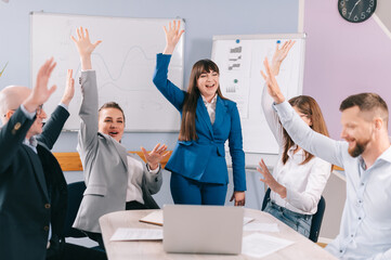 A team of young business people are chanting a team slogan together in the office.