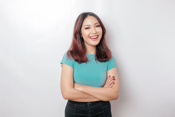 Portrait of a confident smiling Asian woman wearing blue shirt standing with arms folded and looking at the camera isolated over white background