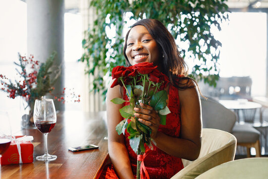 Portrait of a black woman holding a bouquet of red roses while sitting in restaurant