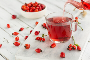 Rosehip glass cup of herbal tea medicinal plants with rosehip fruits pouring glass teapot on table. Dogrose winter tea background
