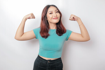 Excited Asian woman wearing a blue t-shirt showing strong gesture by lifting her arms and muscles...